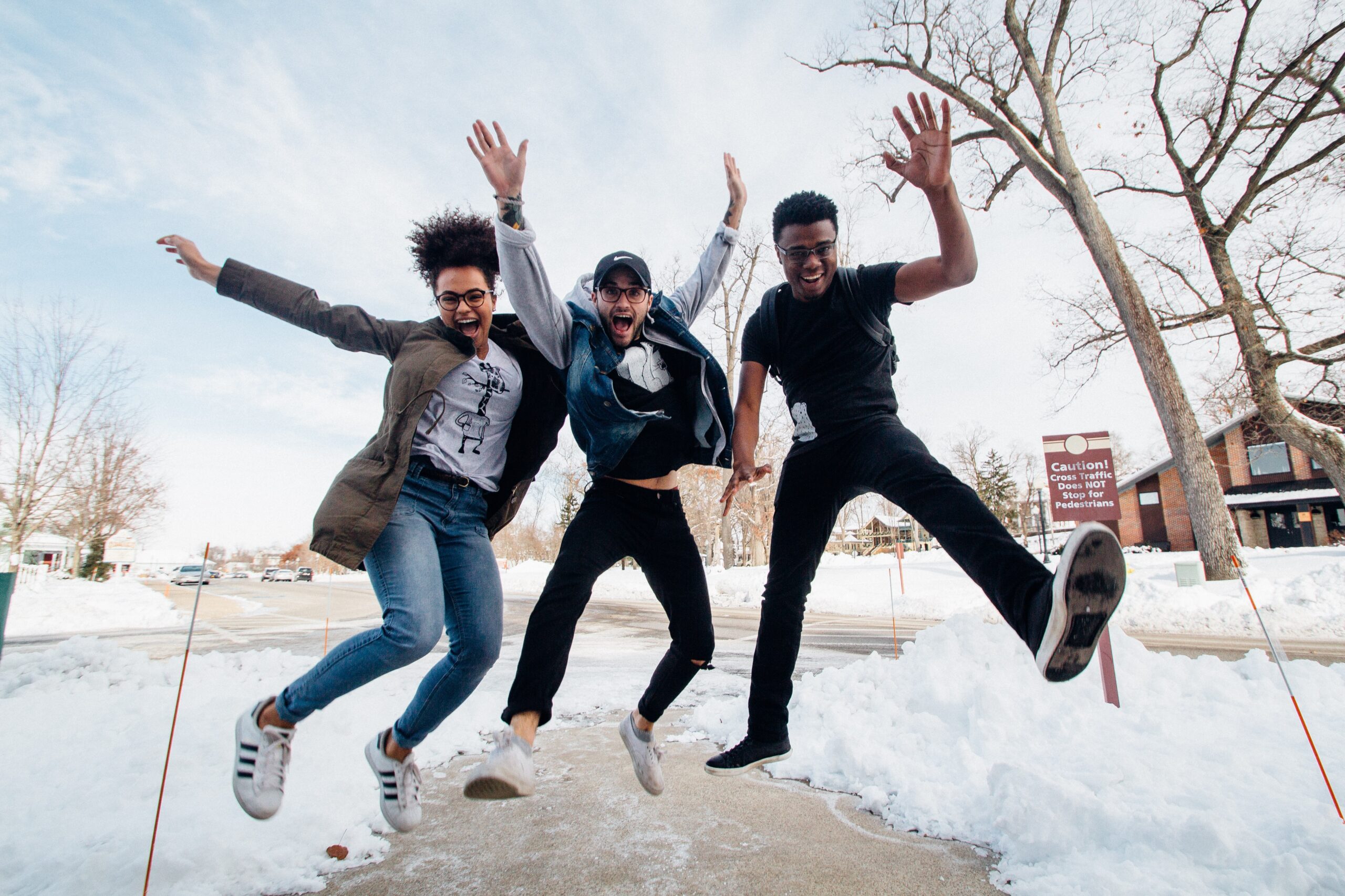 three students of color jumping over a snowy sidewalk with their arms raised in the air