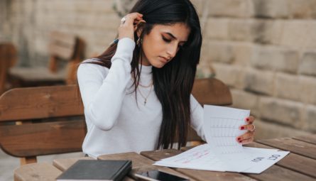 Woman Sitting at Outdoor Table Reviewing Papers With a Notebook Beside Her