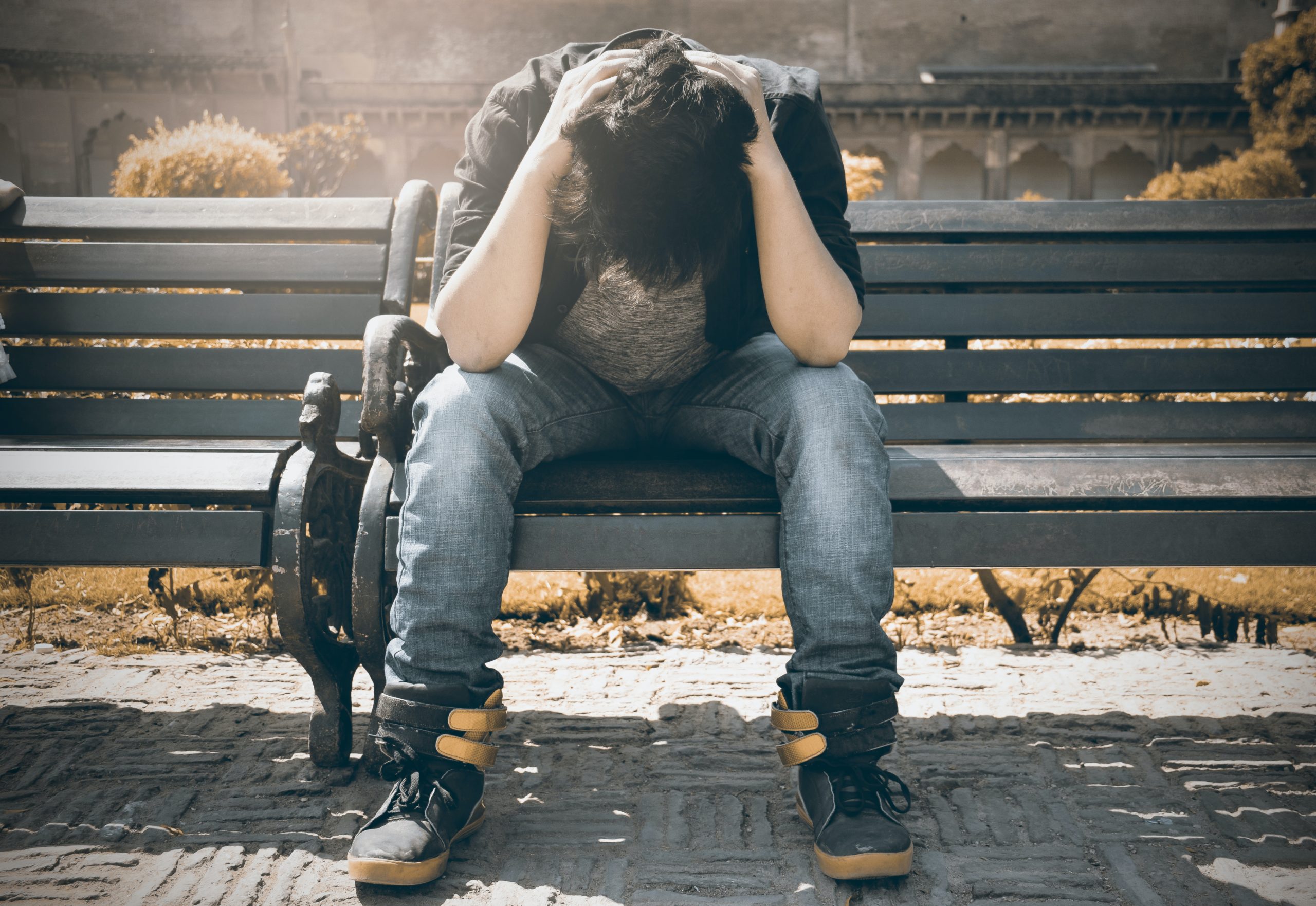 Student sitting on a park bench stressed out with his head in his hands