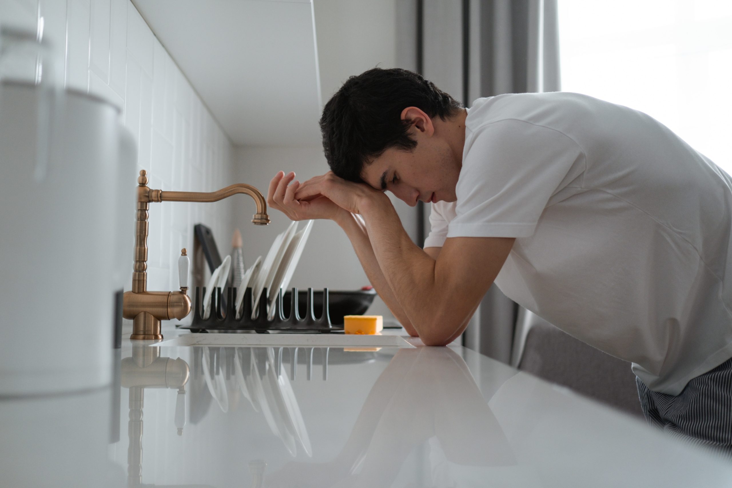 Teen feeling sad, leaning over a kitchen counter with his head in his hands