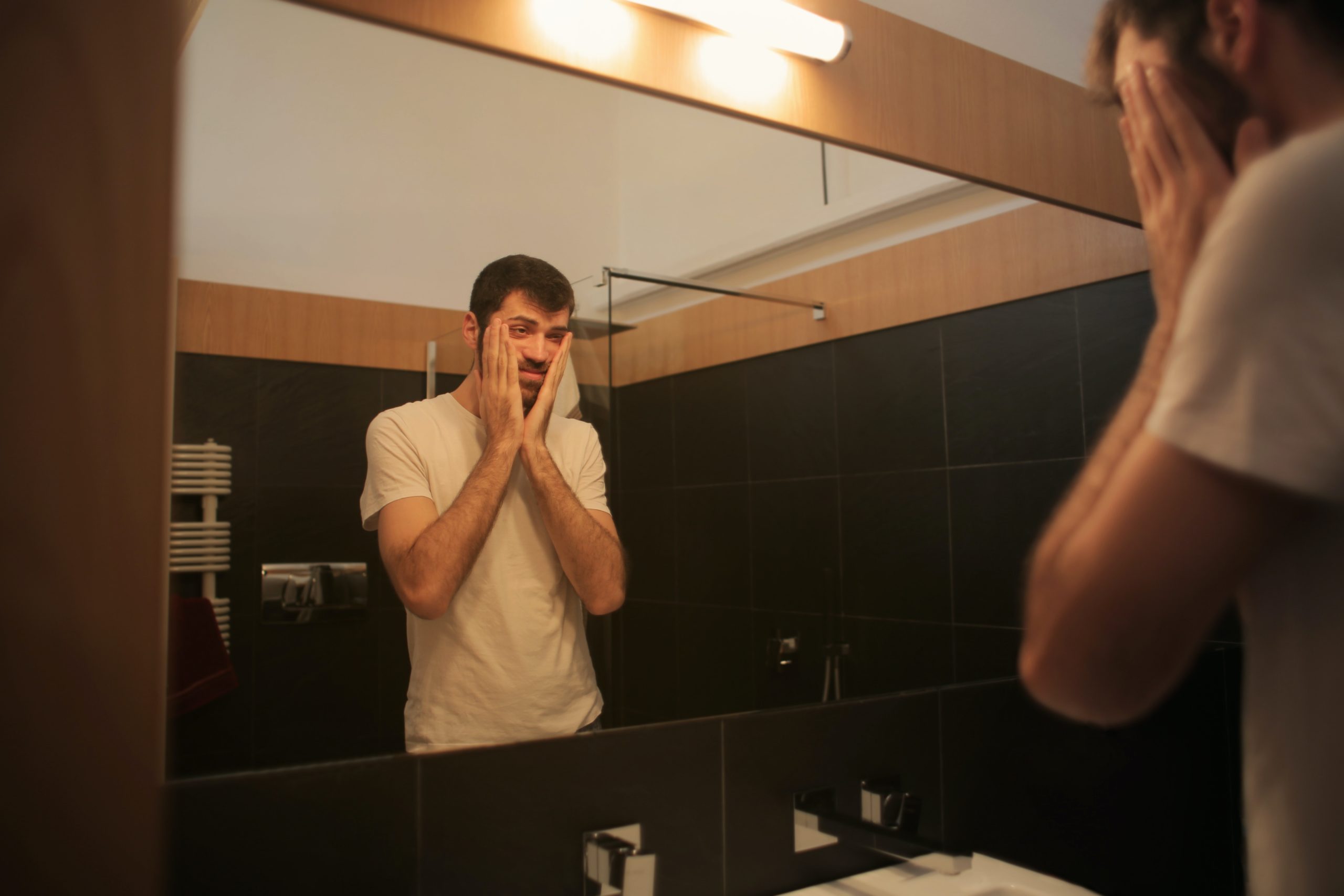 Man struggling with his mental health looking at himself in a mirror in the bathroom