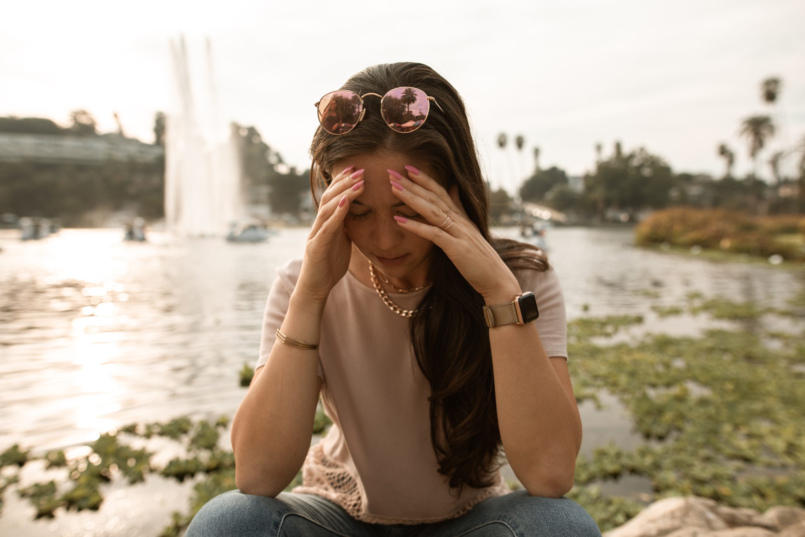 Woman sitting on rocks near a lake with her head in her hands