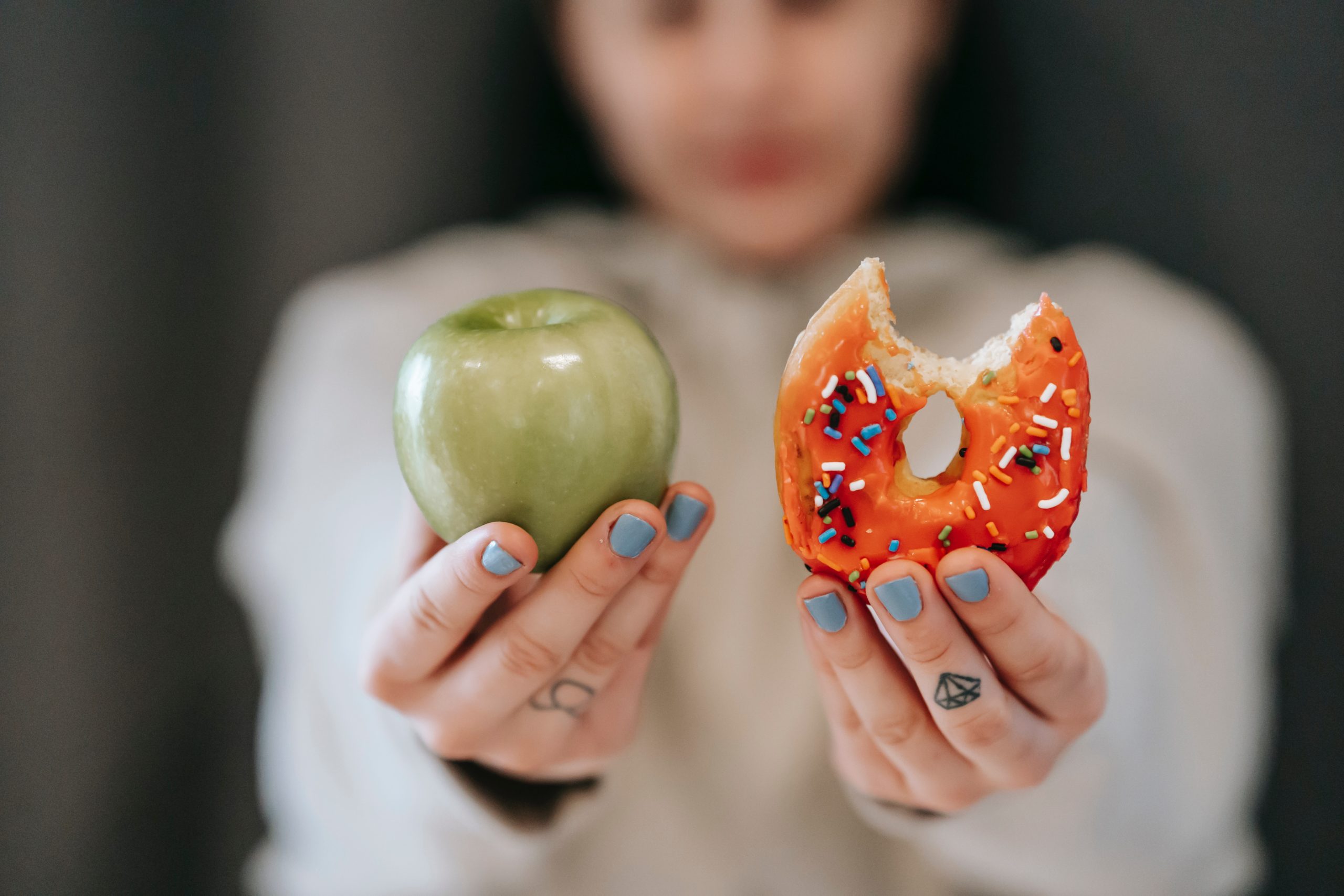 Woman holding up a green apple in one hand and a sprinkle donut in the other