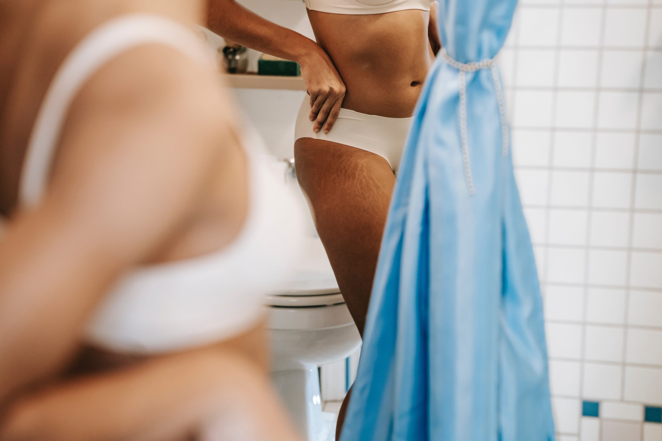 Woman looking at her stretch marks in a bathroom mirror