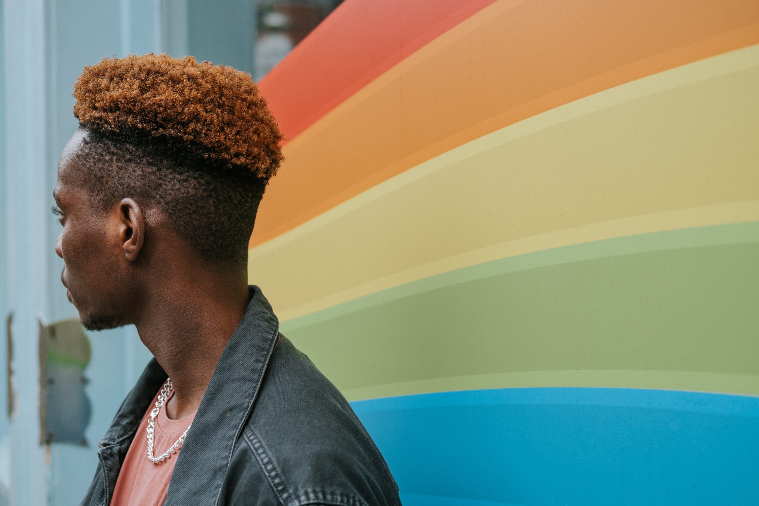 Man looking to the side, standing in front of a rainbow backdrop