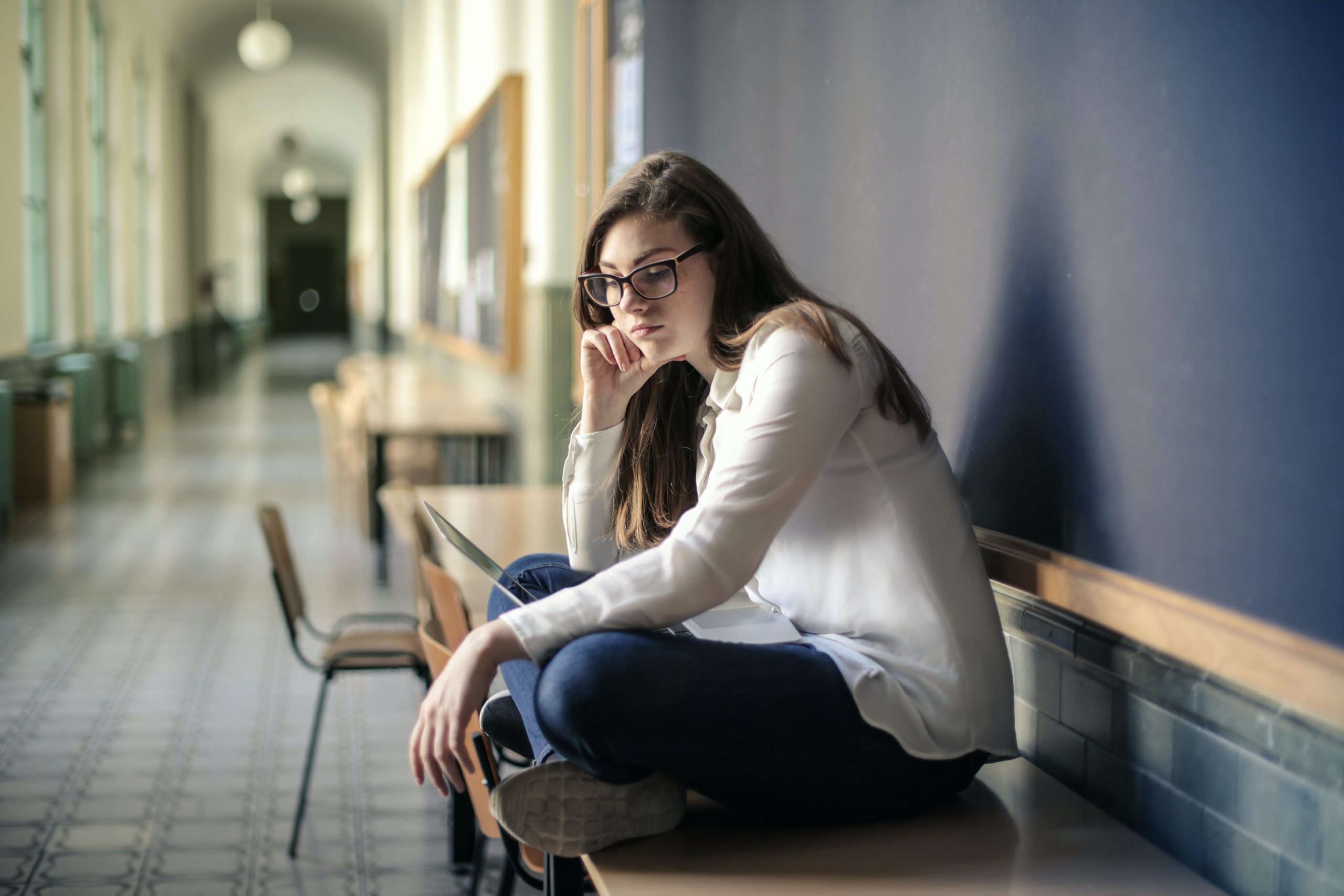 Student sitting alone with her computer in her lap, looking into the distance
