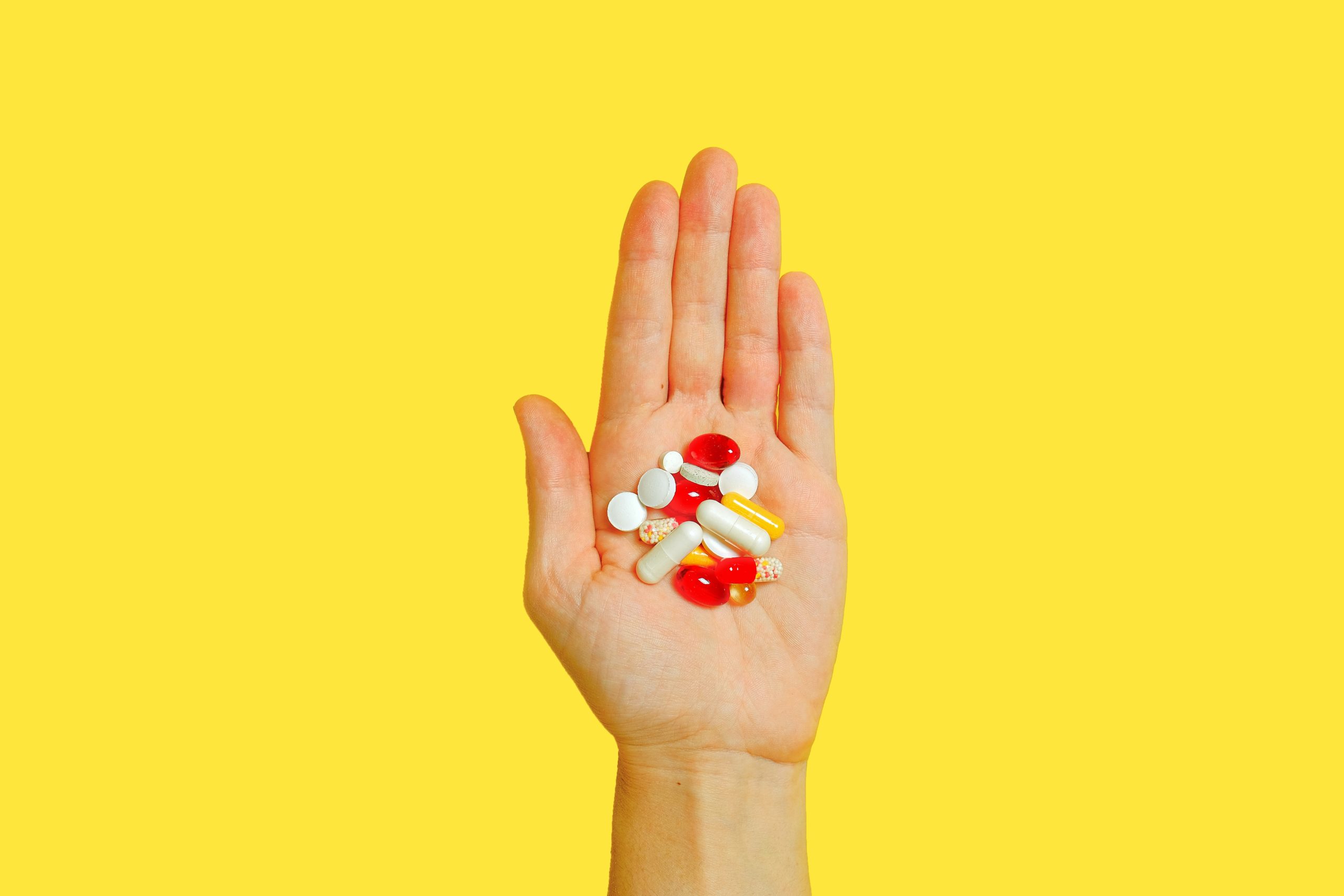 Hand holding pills over a yellow backdrop