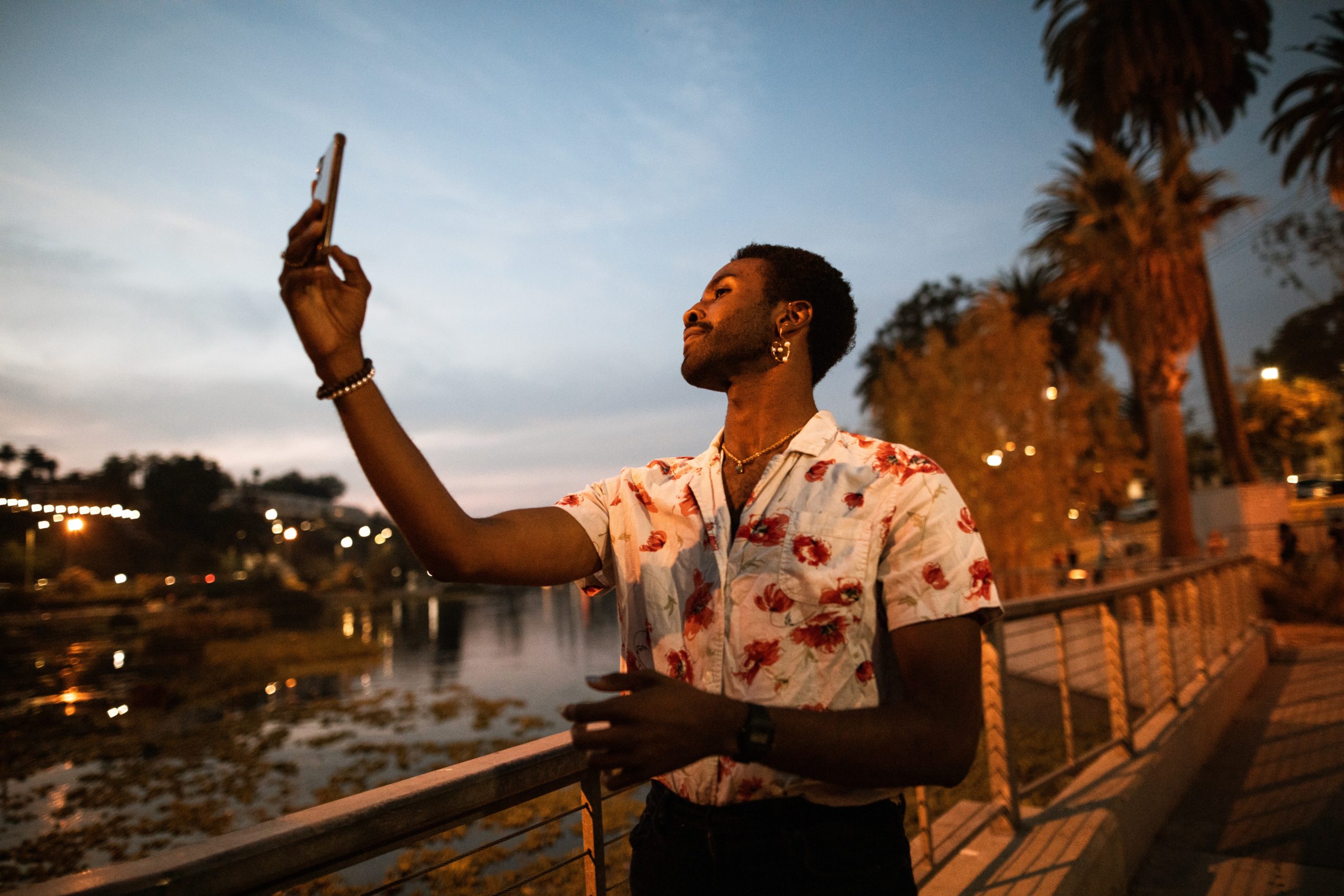 Man standing outside near palm trees and water talking a selfie