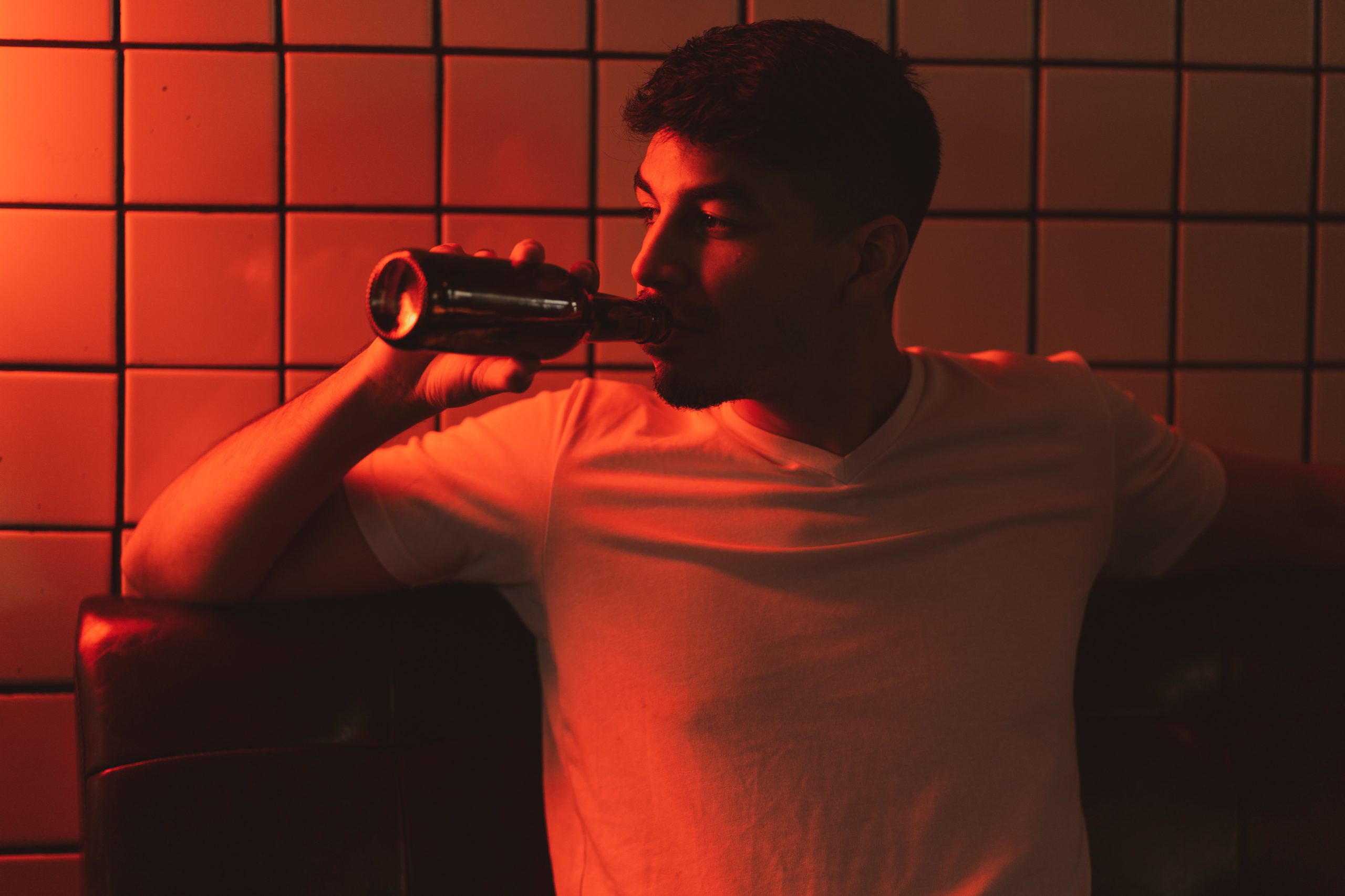 Man sitting in a room with red lighting drinking a beer