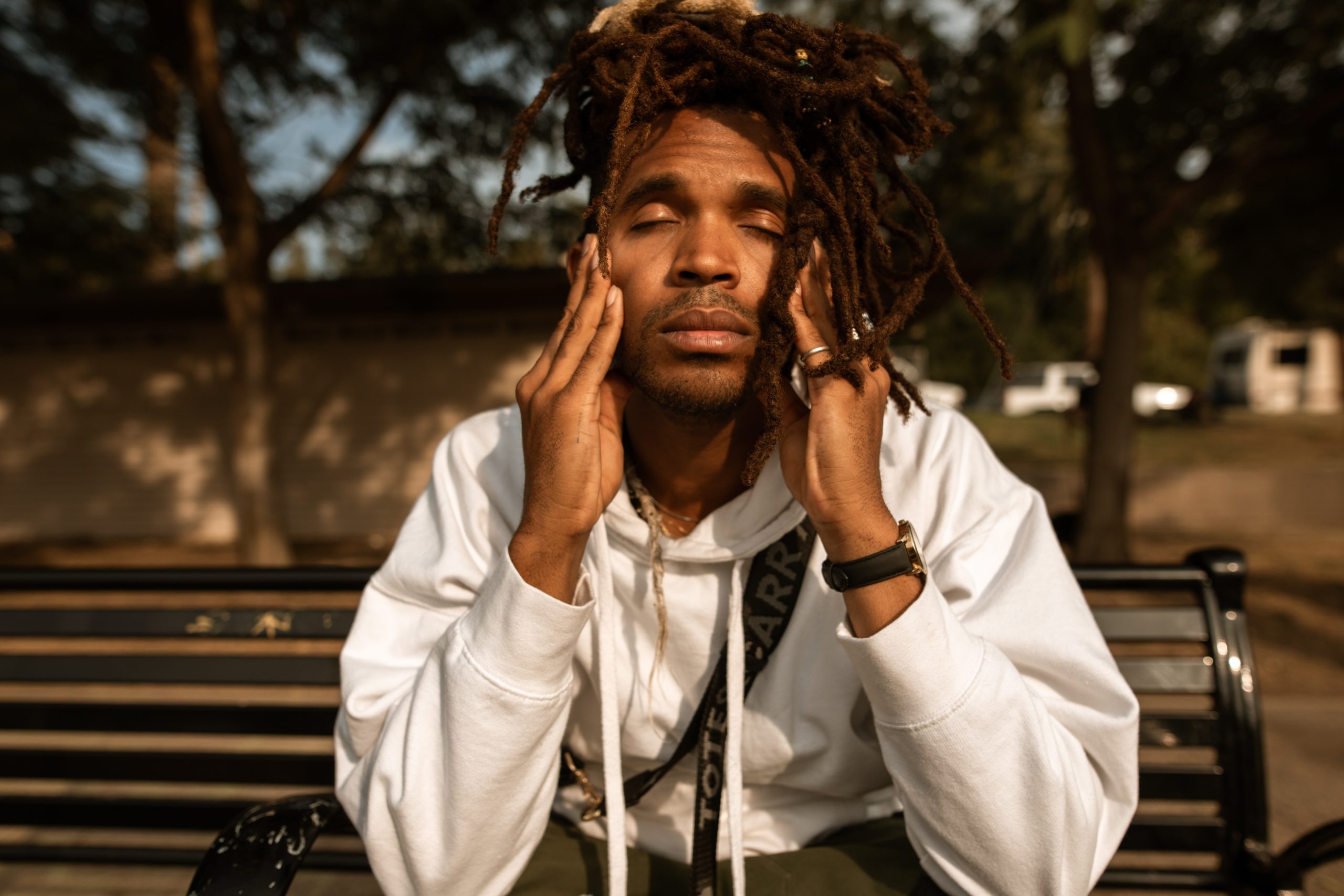 Man sitting on a park bench with his eyes closed massaging his temples