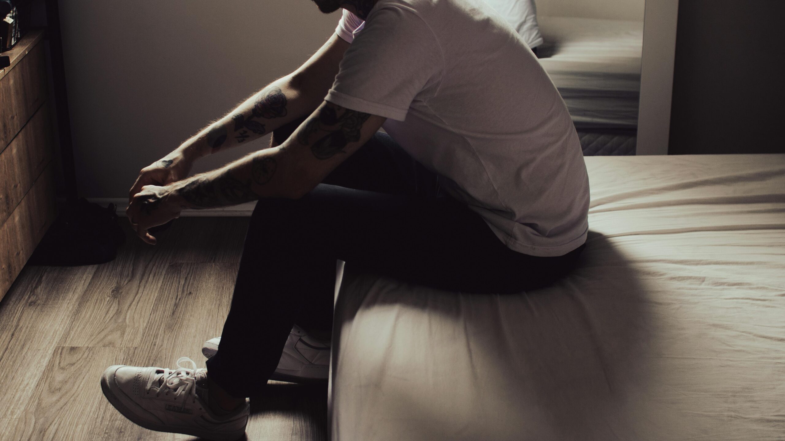 young man sitting on his bed with his arms on his knees