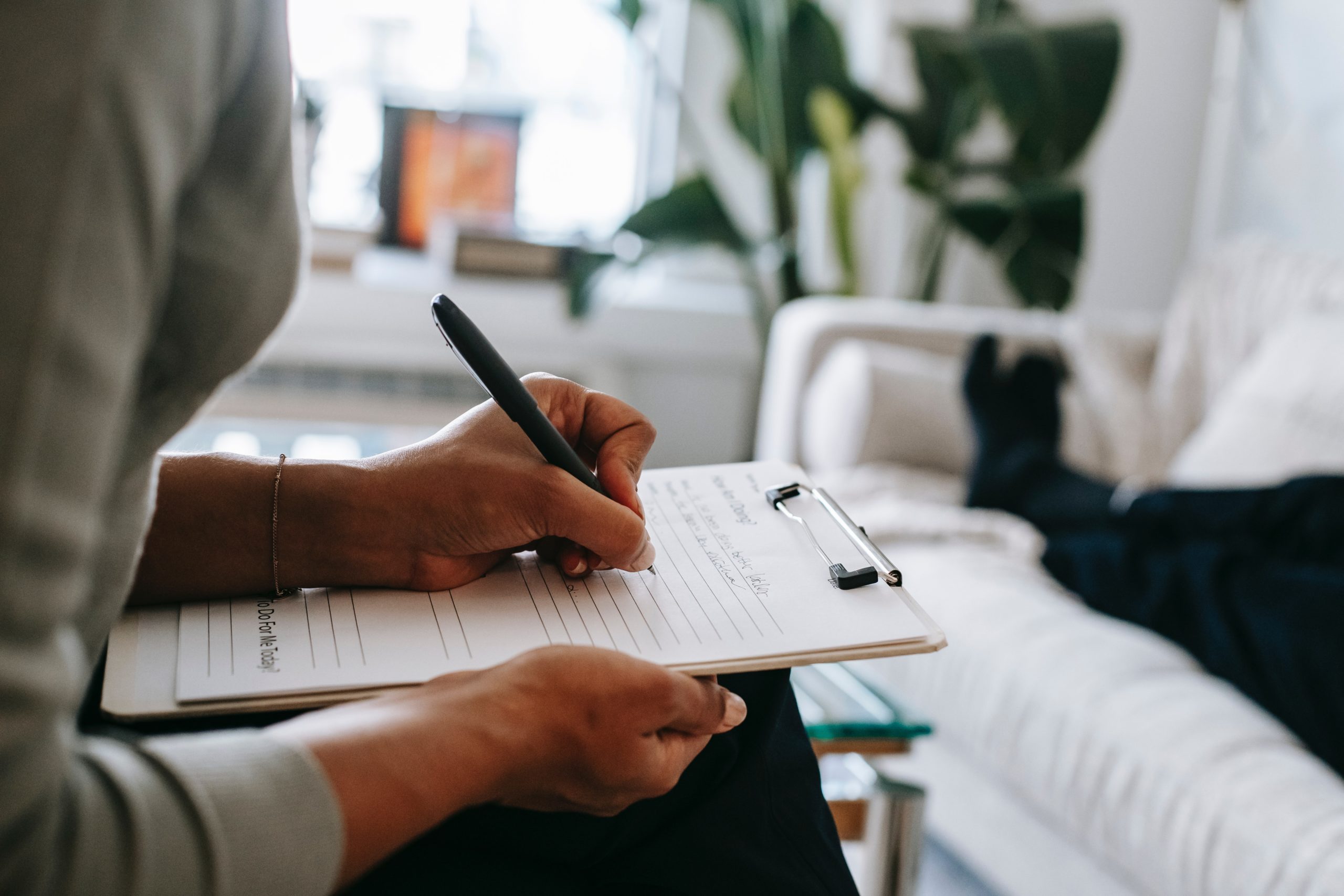 therapist writing notes on intake sheet while patient's legs are stretched out on couch