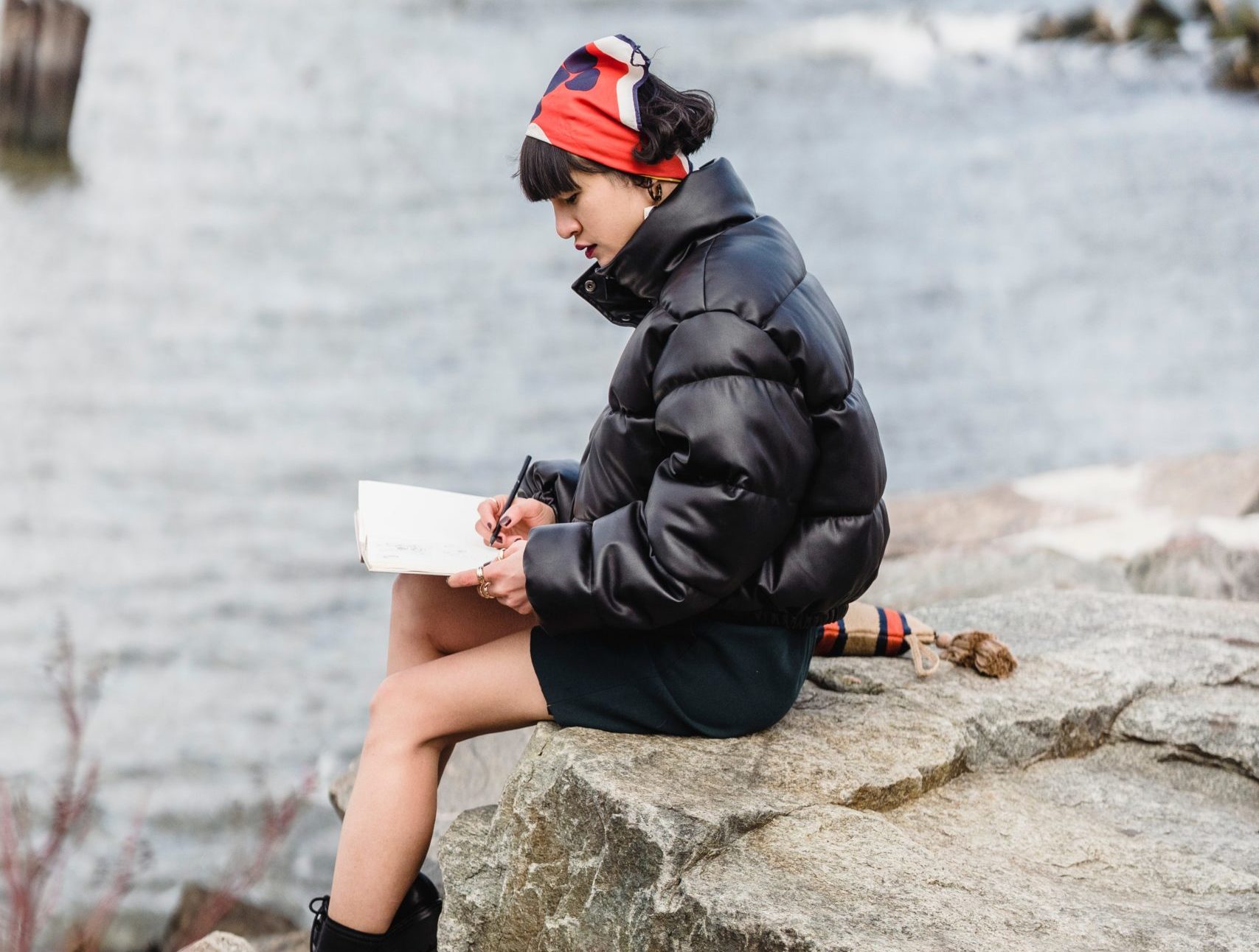 woman sitting on a rock ledge overlooking water journaling