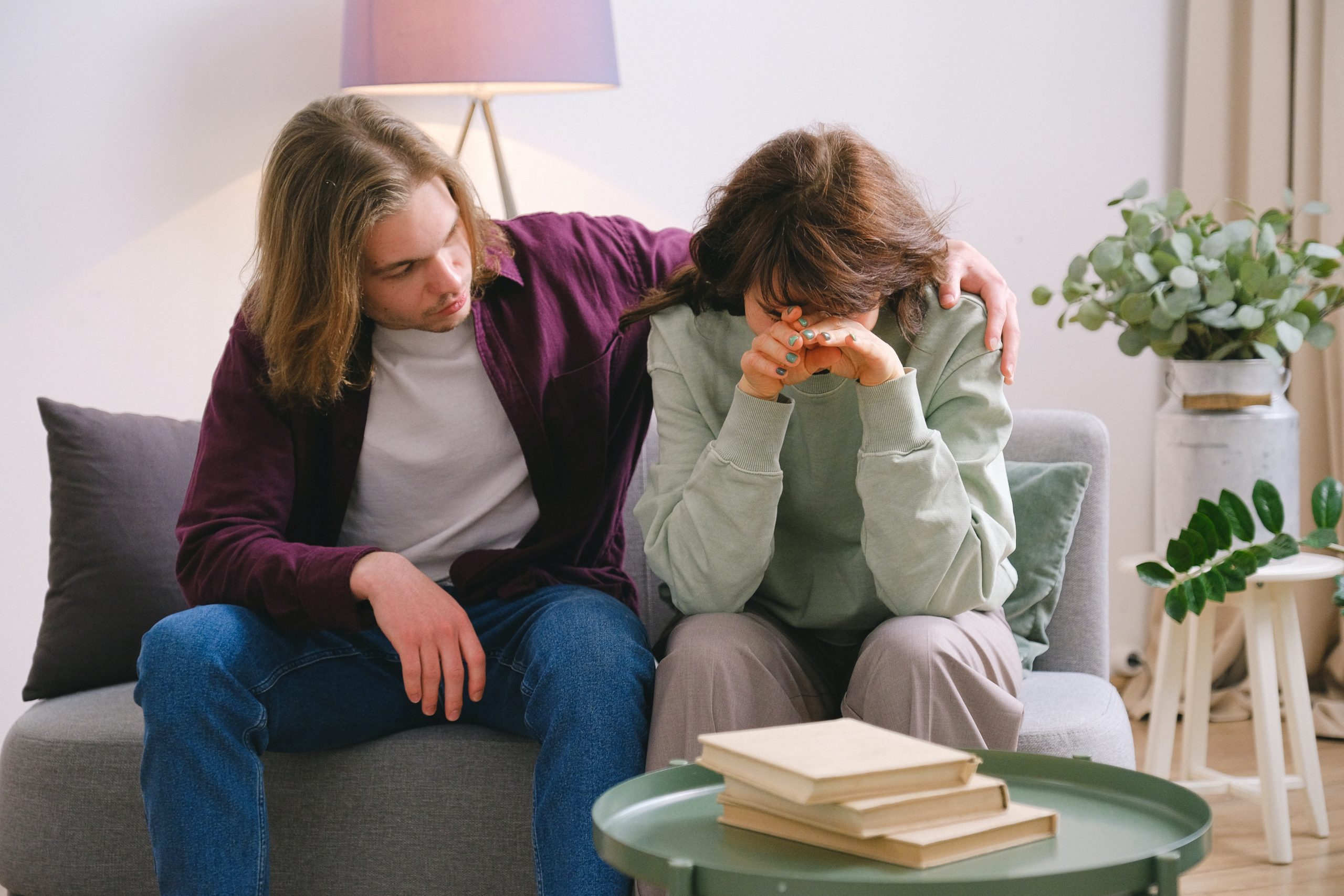 Young male comforting upset woman on a couch who had her hands covering her face