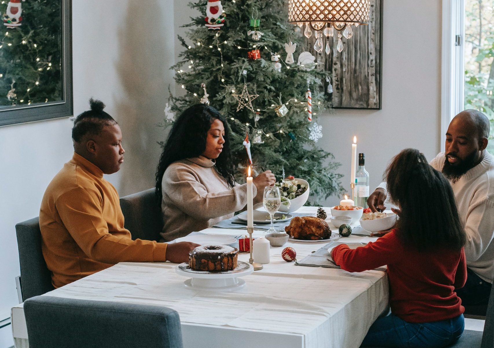 black parents teen and young child having candlelight dinner at the table with decorated christmas tree