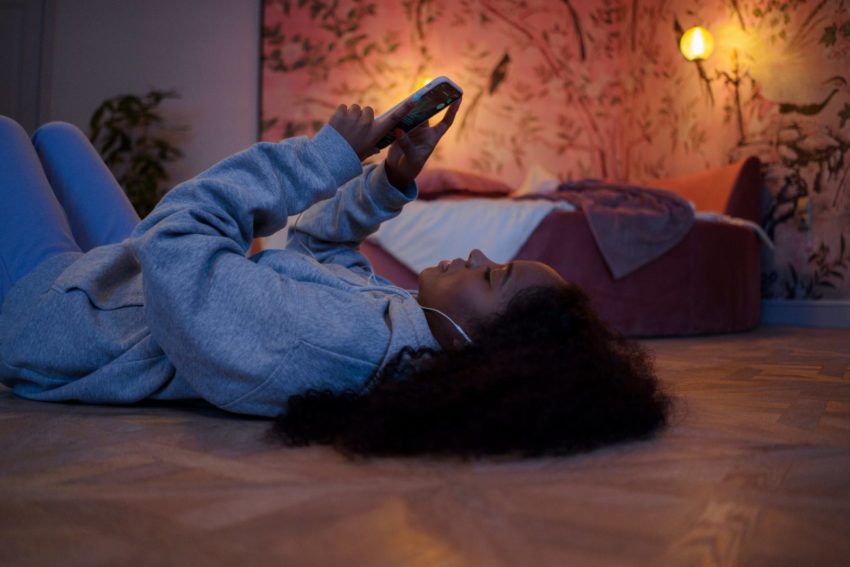 Black student with wavy black hair holding phone in dim lit room
