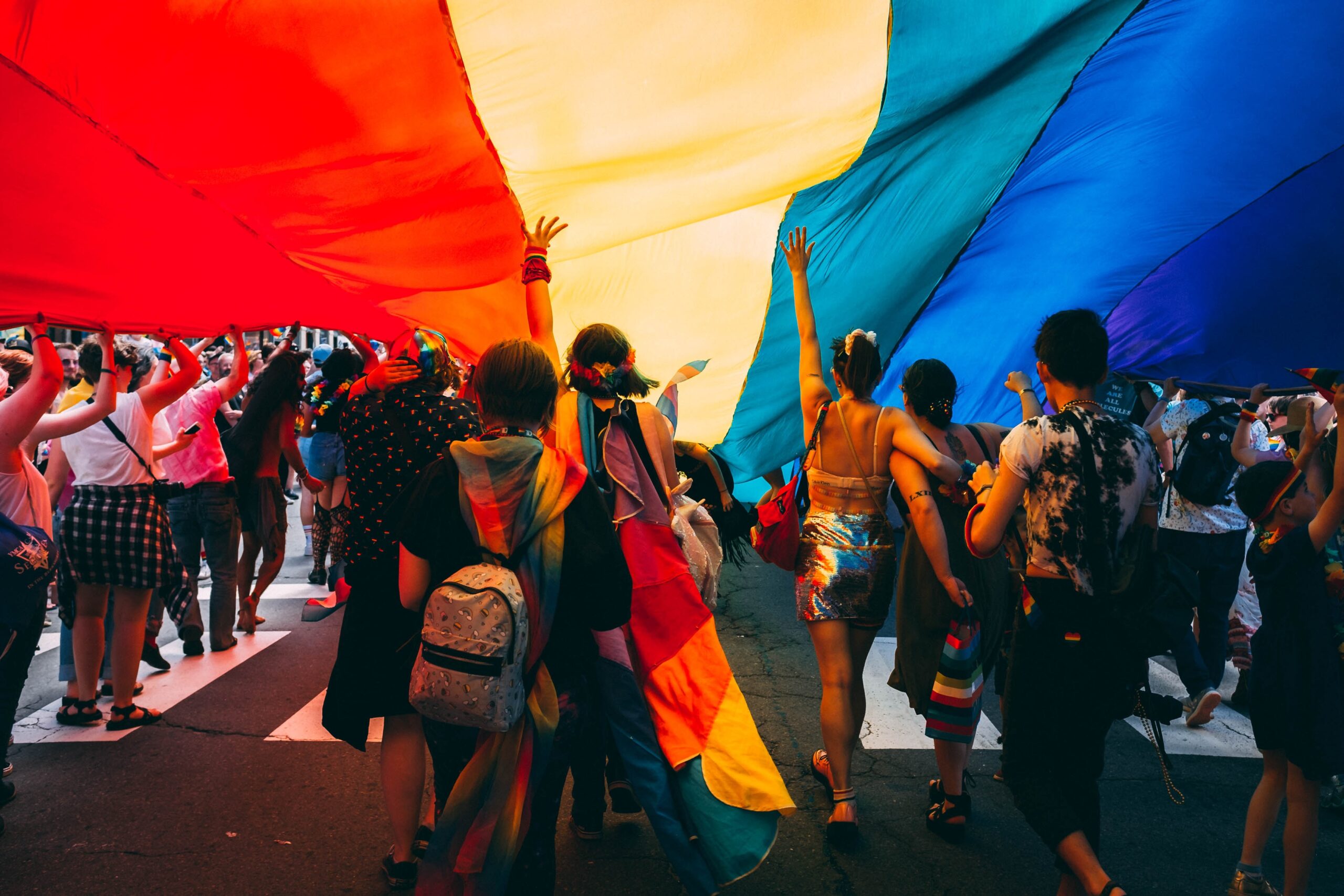Group of young adults gathered under a large Pride flag