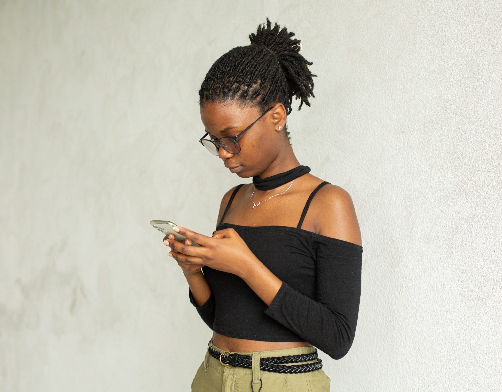 student with braided pony tail and glasses standing up looking at her phone with a serious look on her face