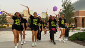 group of students walking and dancing in the street while wearing black shirts with neon green writing neon nights
