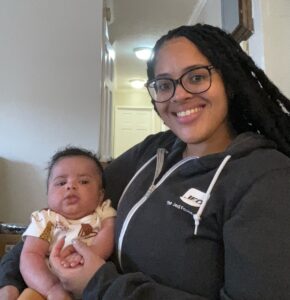 student parent Brenda Leger wearing JED sweatshirt, smiling while holding baby