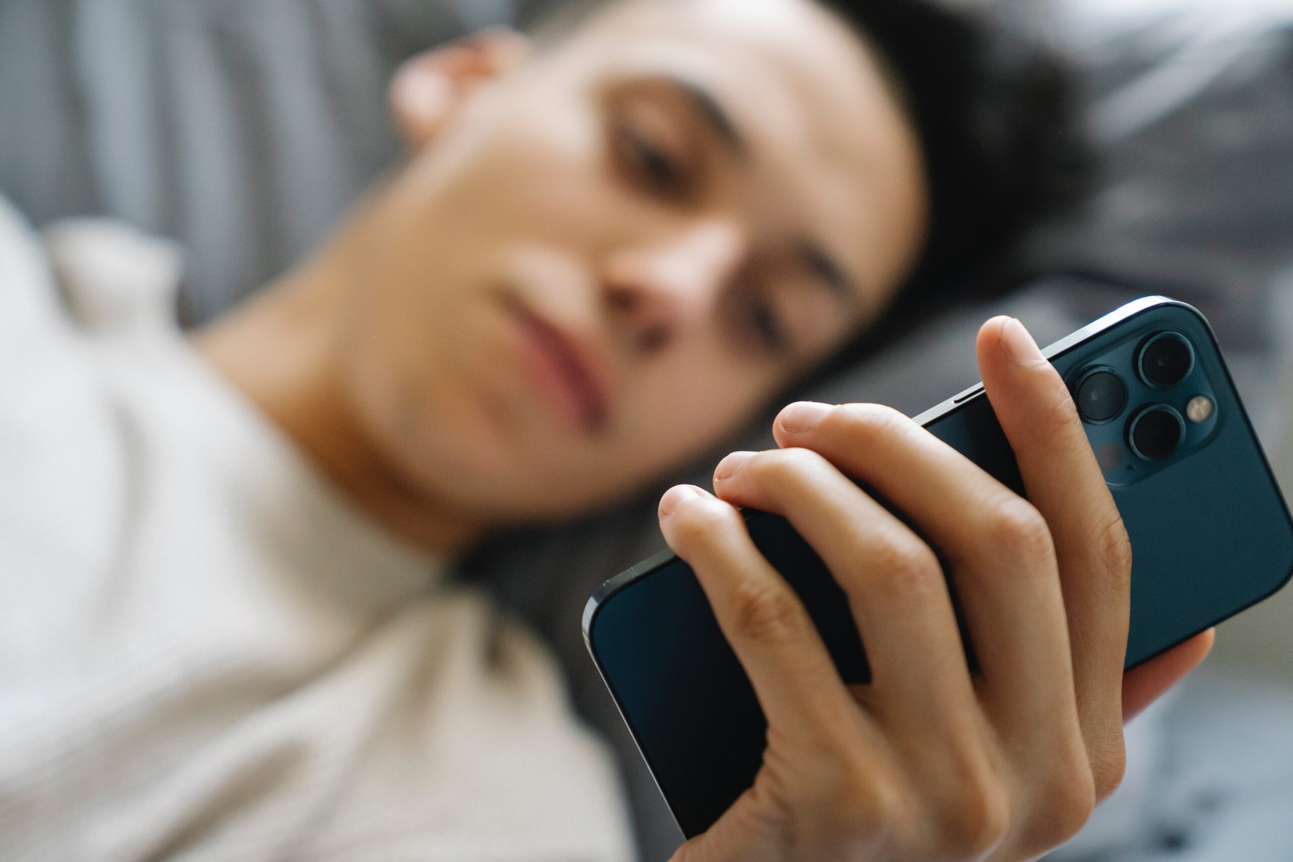 young man holding phone in bed