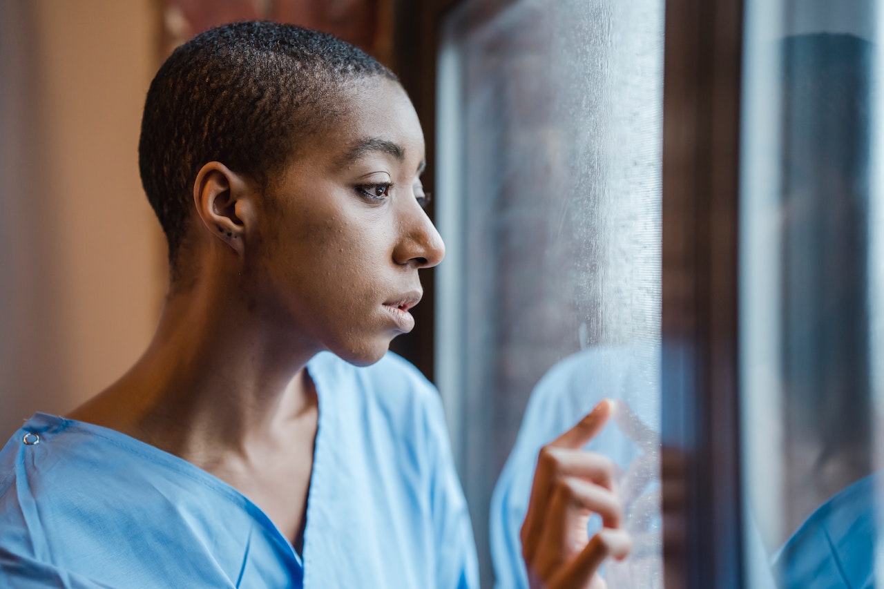 Young woman in scrubs looking out the window with her finger on the glass