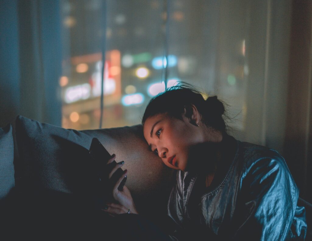 Student sitting in the dark on the couch with sad look on her face while looking at her cell phone