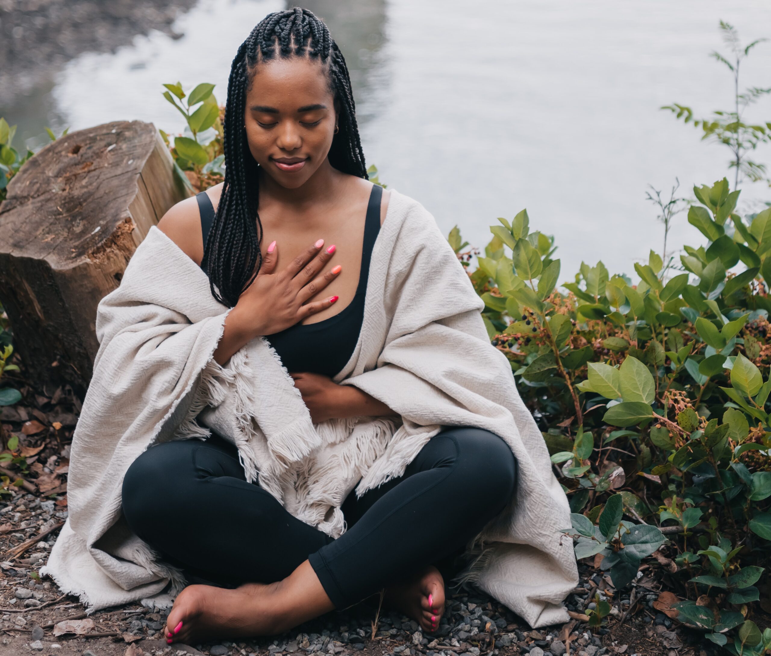 black woman with eyes closed sitting in front a lake mediating