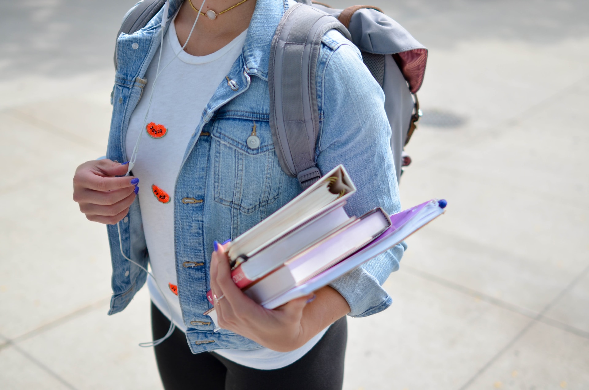 student standing with book bag, holding books on college campus