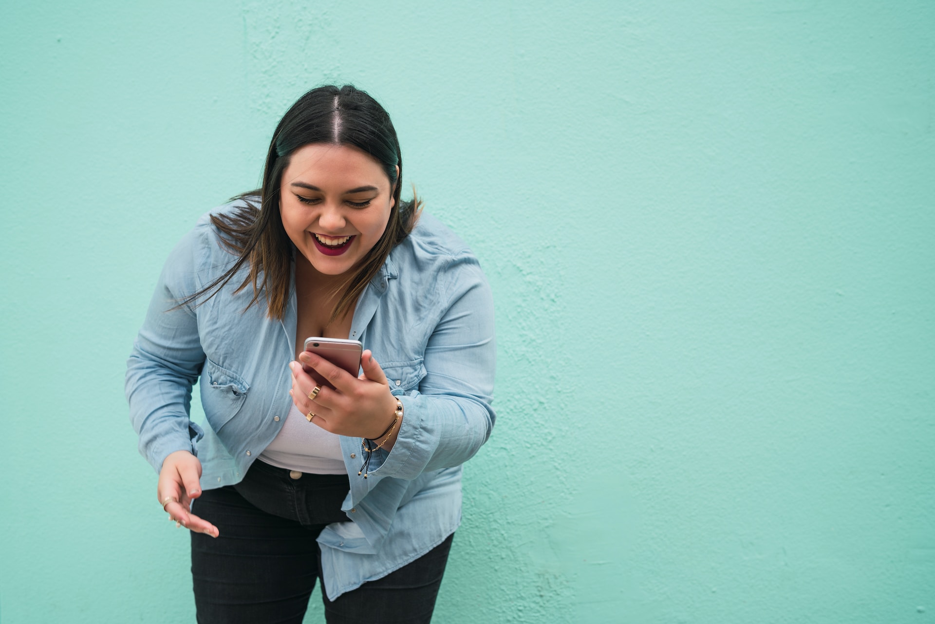 young woman leaning forward laughing while looking at the phone in her hand