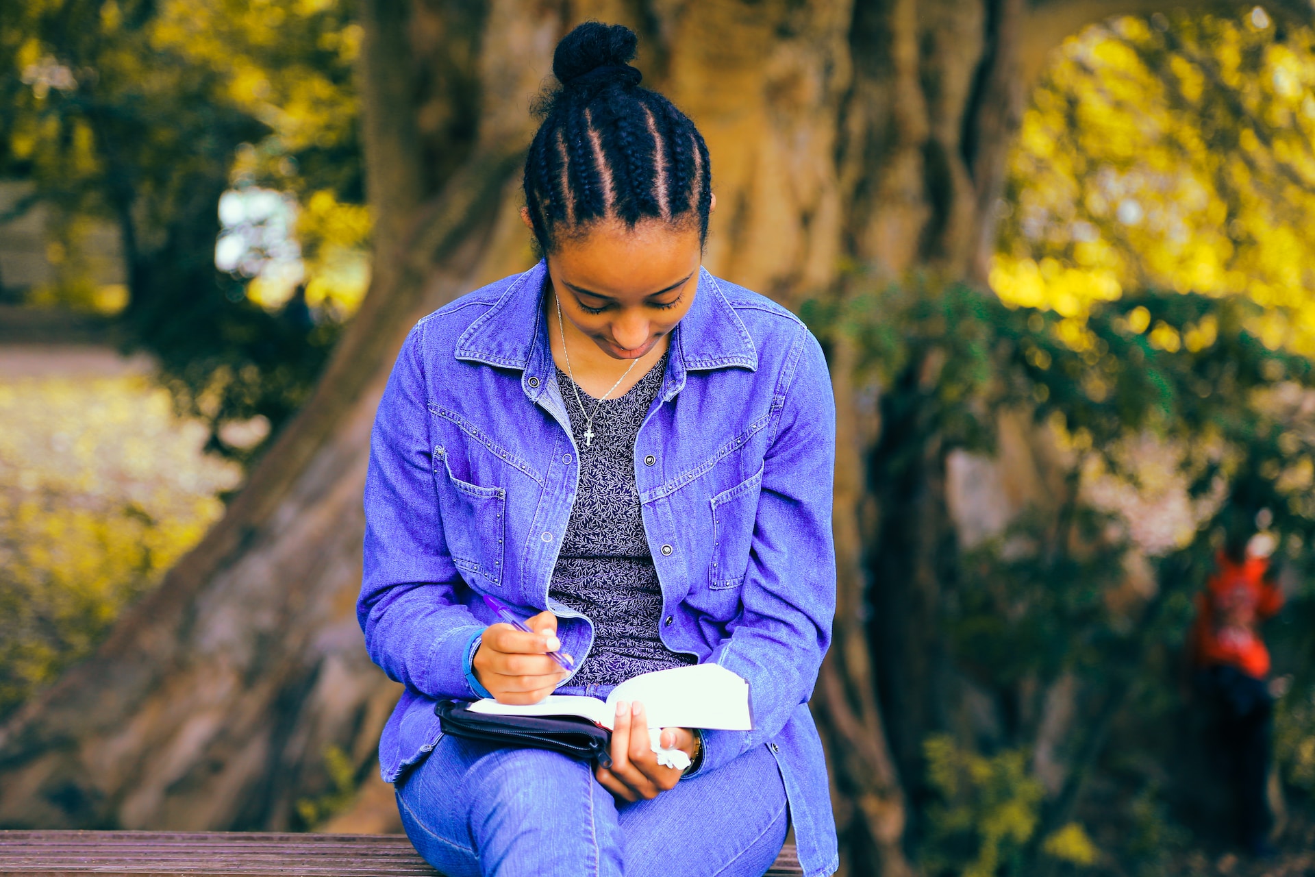college student sitting in front a tree writing in a notebook