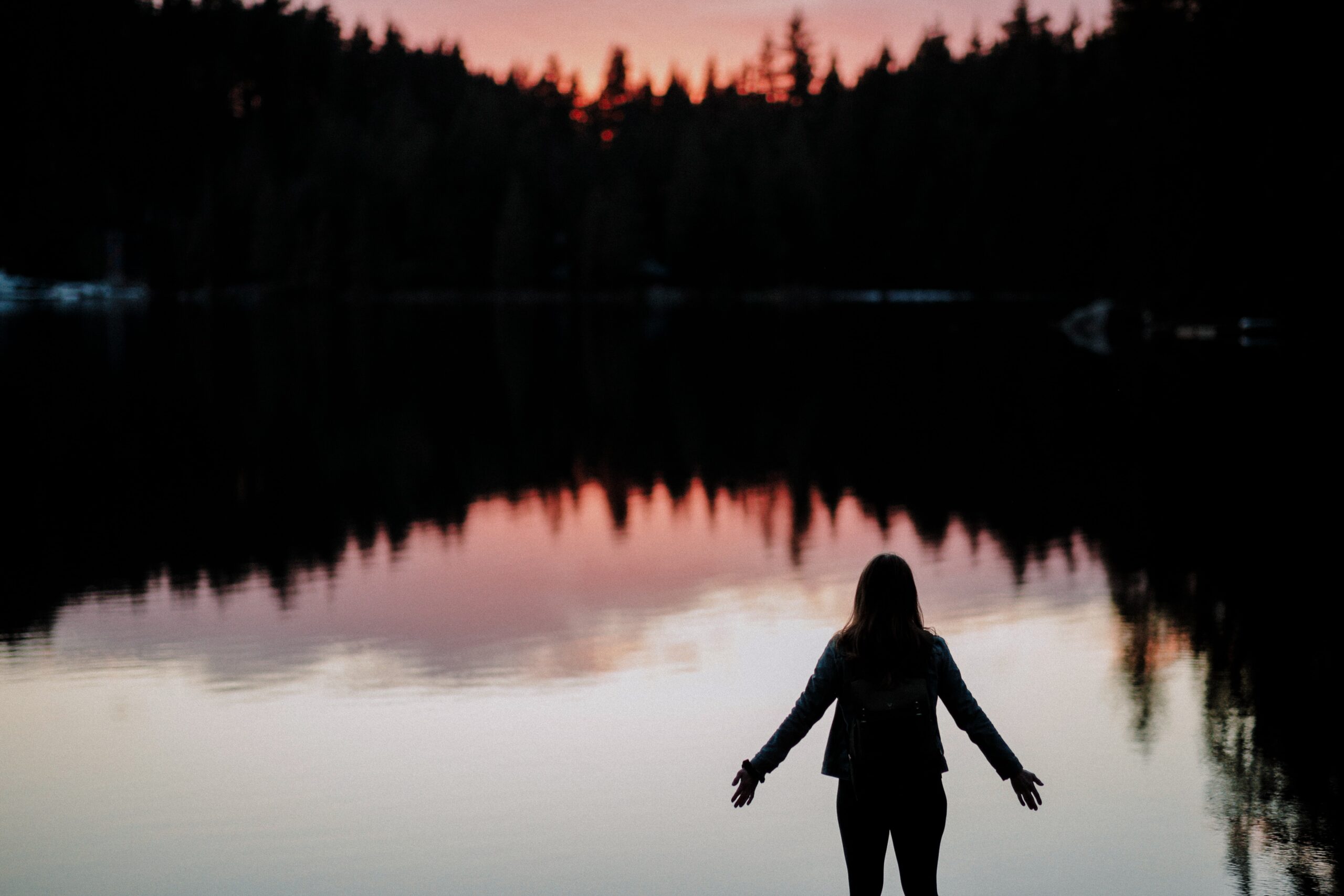 The silhouette of a woman overlooking a serene lake surrounded by trees