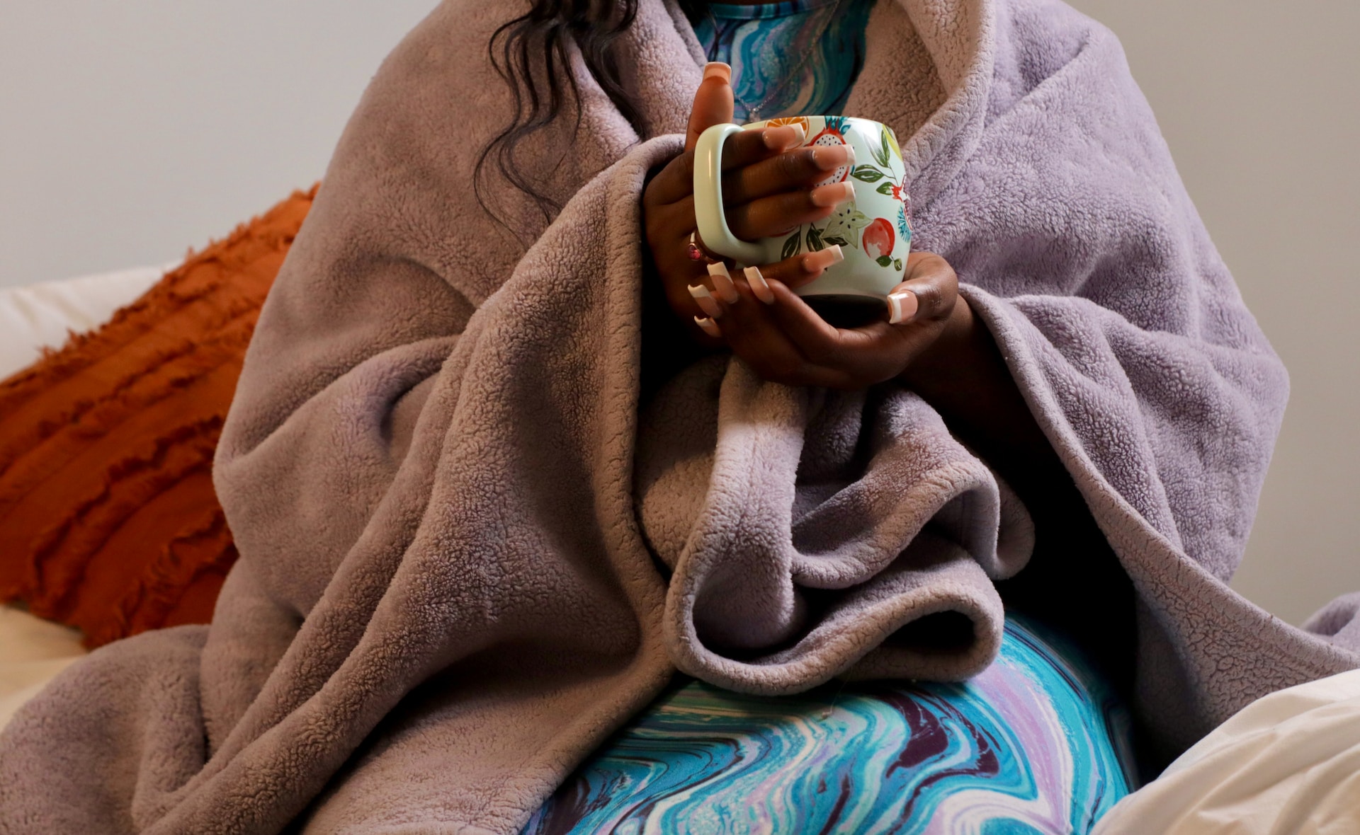 student sitting on the bed wrapped in a blanket and holding a cup of tea as part of her self care in college
