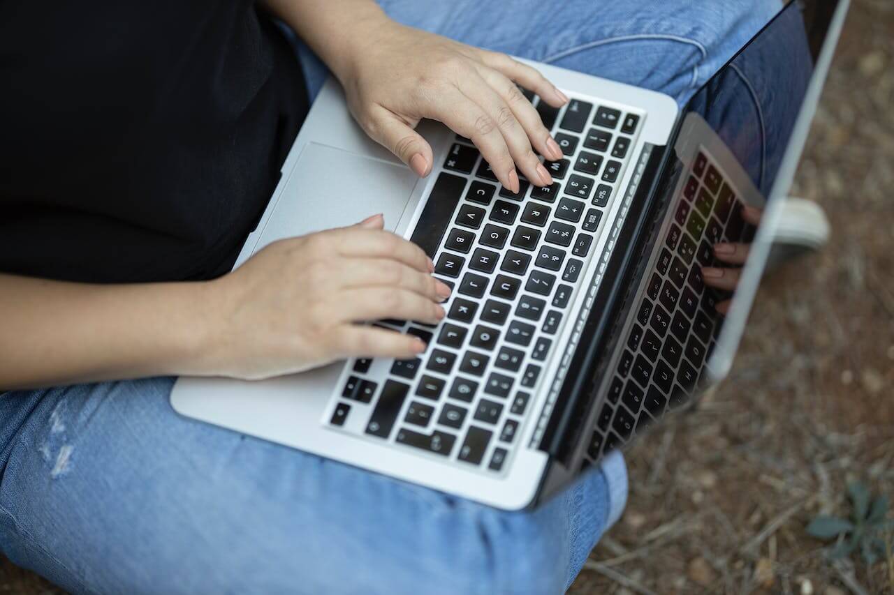 Teen sitting down outside with laptop in their lap and fingers typing on keyboard