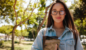 young woman wearing glasses walking outside holding books in her hand