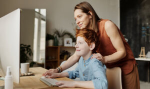 young boy working on the computer with his supportive parent standing behind him