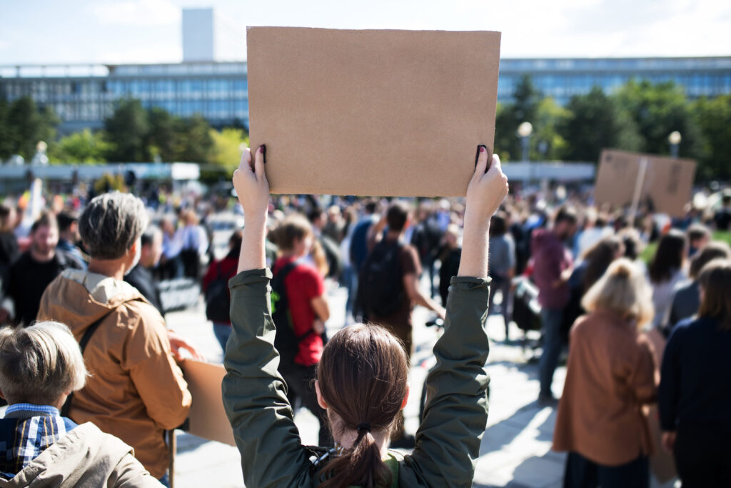 A person standing outside in a crowded area holds up a cardboard sign as part of a peaceful protest.