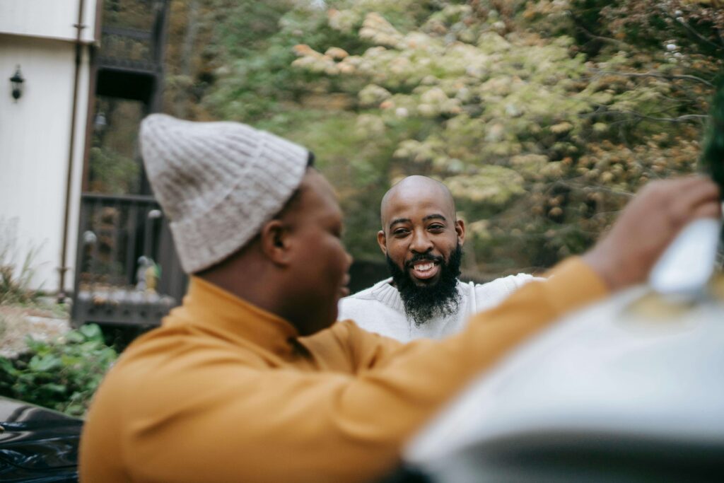 A parent and teen engaging in a conversation outside while leaning on a car.