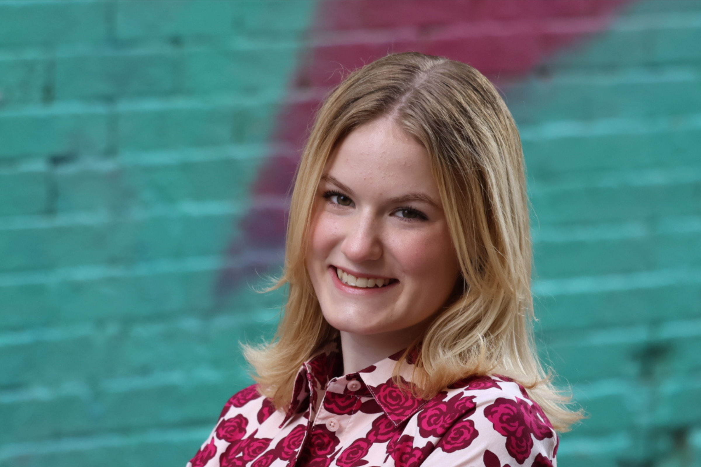 A teen girl poses in front of a spray painted brick wall