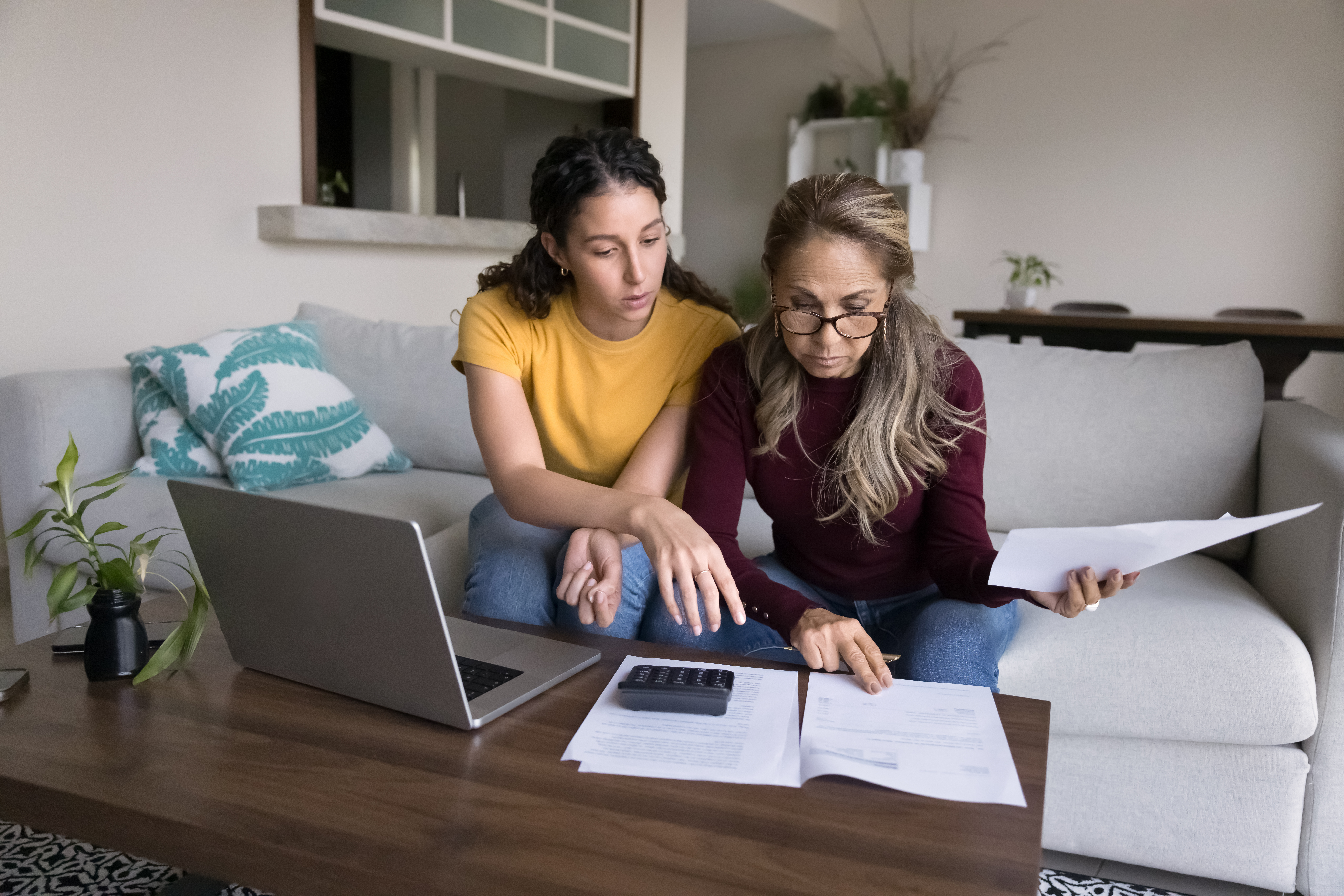 A young adult woman and her mother are sitting on a couch looking over their finances